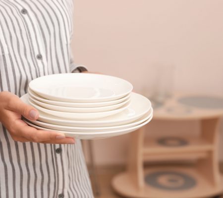 Woman holding stack of clean dishes in kitchen, closeup. Space for text